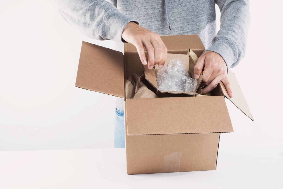 Hände verpacken ein Produkt sorgfältig in einen Versandkarton